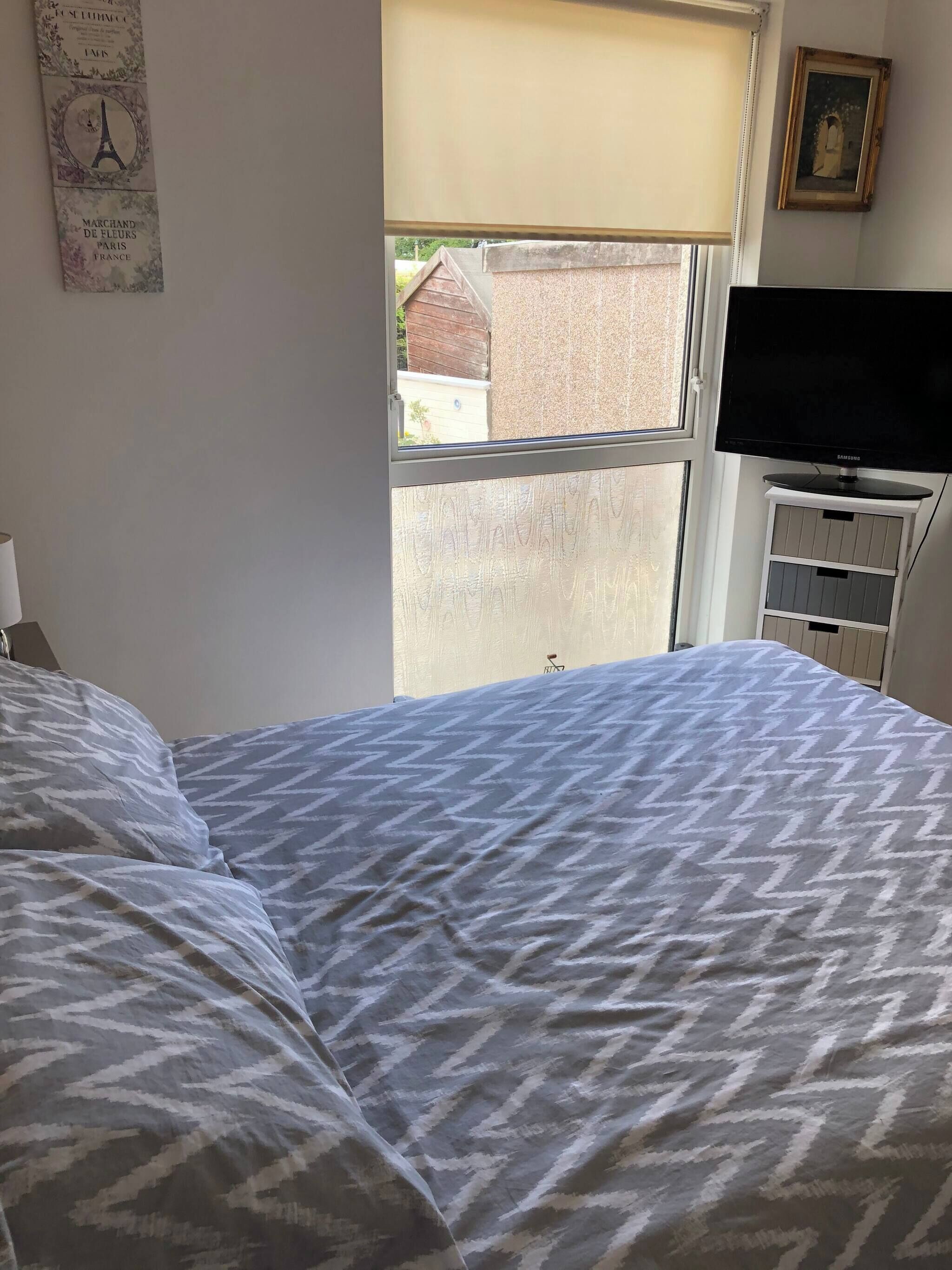 Een slaapkamer met een bed, een raam, een televisie en een dressoir.