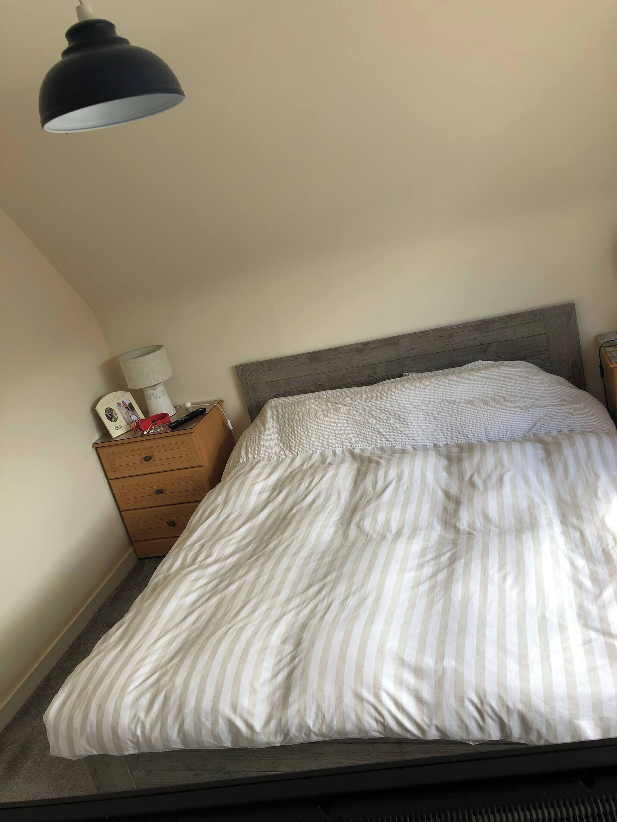 A bed with a striped white and gray comforter, a wooden nightstand with a lamp, and a wooden headboard.