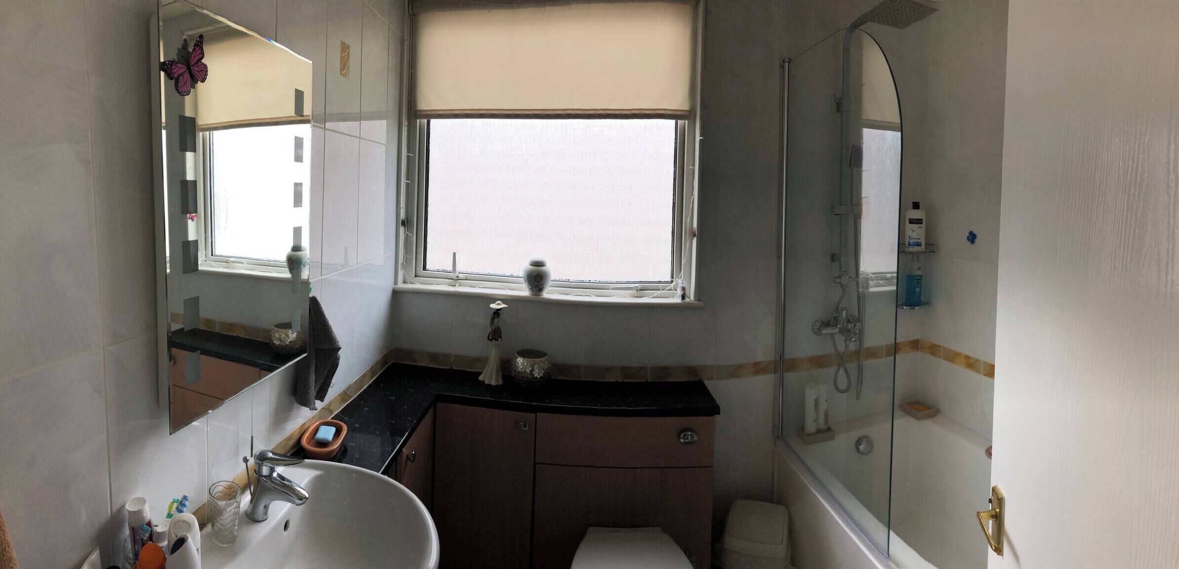 A bathroom with a sink, mirror, vanity, window, and shower.