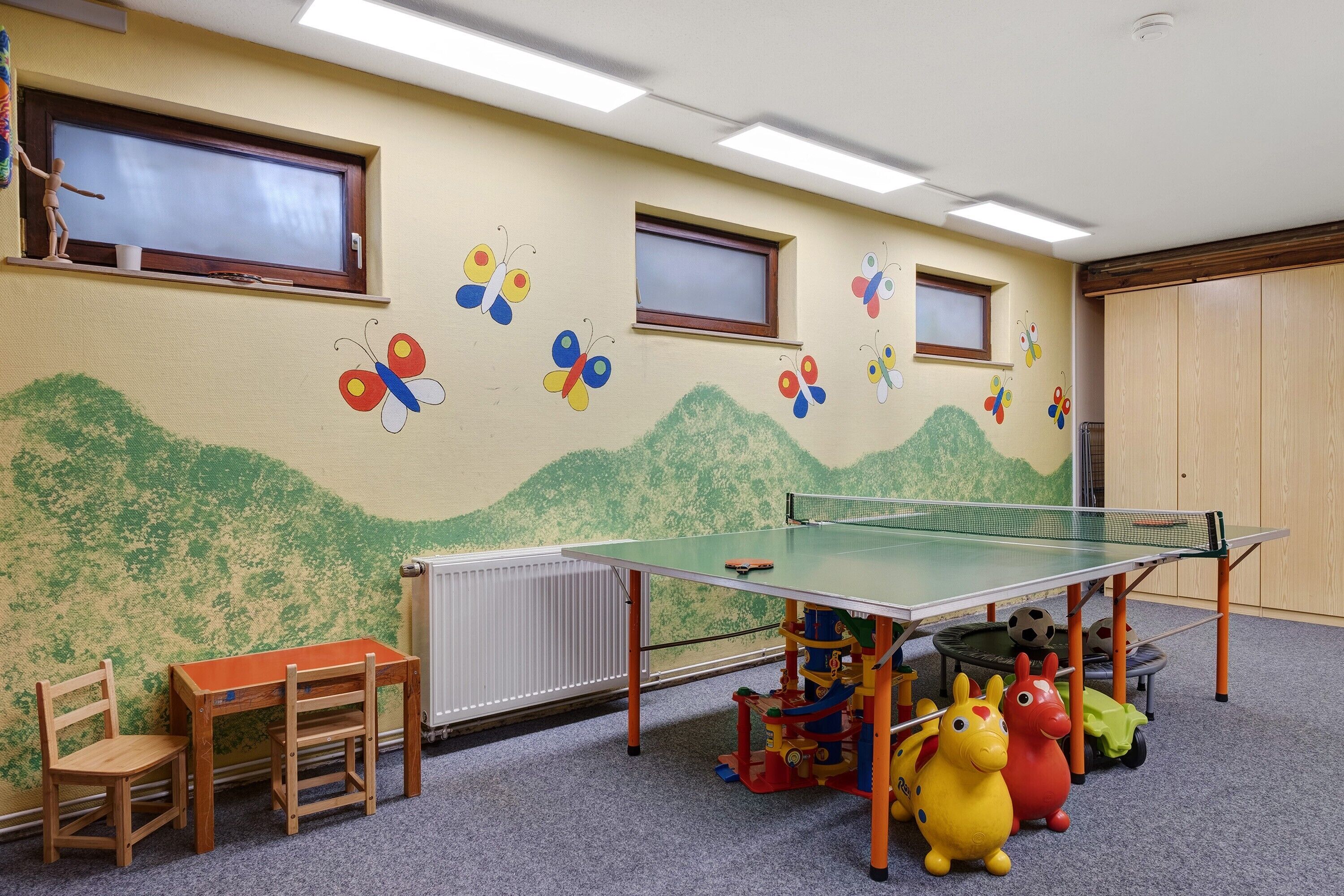 A children's playroom with a ping pong table, chairs, and a mural with butterflies.