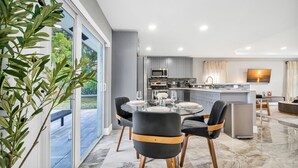 Una cocina moderna con armarios grises, una isla central y un comedor con mesa y sillas de vidrio.