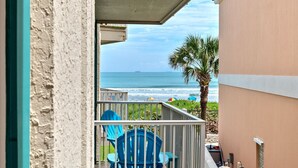 Ein Balkon mit Blick auf das Meer, einer Palme und blauen Stühlen.