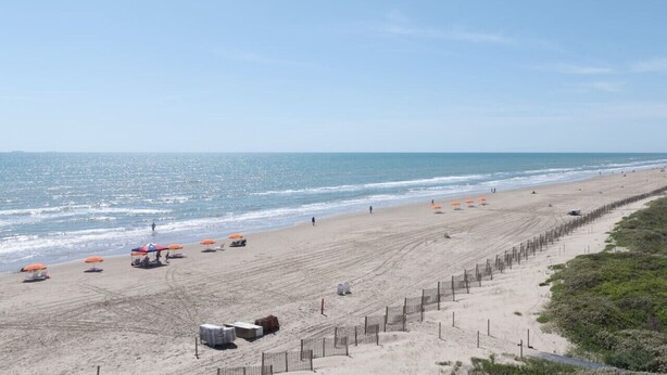 Ein Strand mit Sonnenschirmen, einem Zaun und blauem Himmel.
