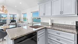 A modern kitchen with white cabinets, granite countertops, and a view of the water. - Luxury 168 Long Island Village (Port Isabel)