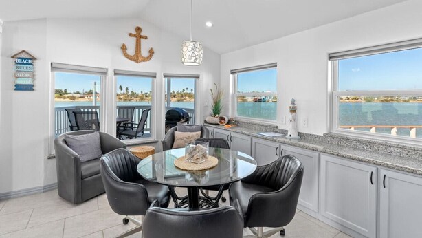 A modern kitchen with a view of the water, a dining area with chairs, and a bar area with a grill. - Luxury 168 Long Island Village (Port Isabel)