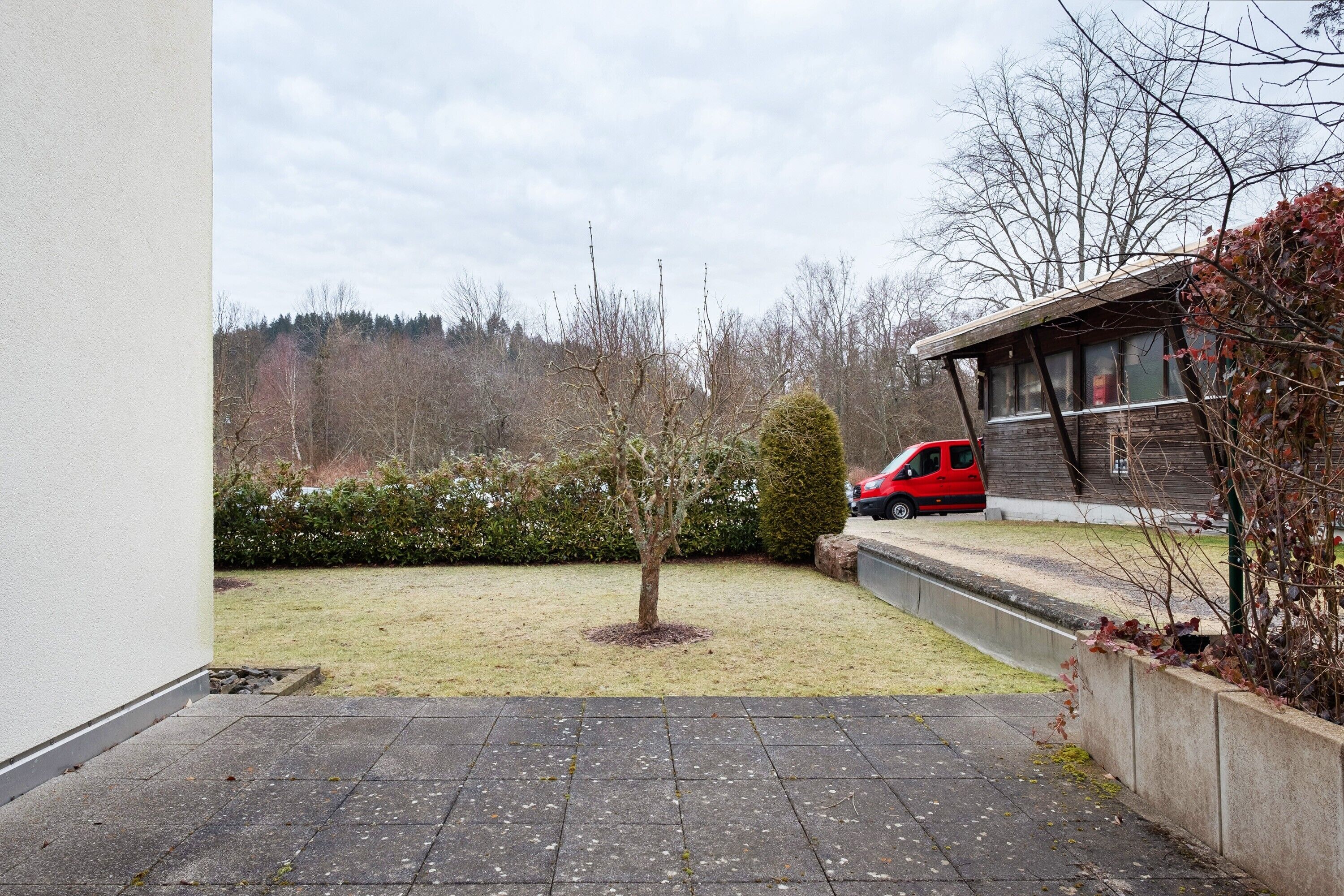 Een geplaveid binnenterrein met een kleine boom, een rode auto die er geparkeerd staat, en een gebouw met een schuin dak.