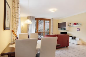 A living room with a red sofa, a dining table with chairs, a TV, and a bookshelf. - Apartment 'No. 3c' with Private Terrace and Wi-Fi (Titisee-Neustadt)