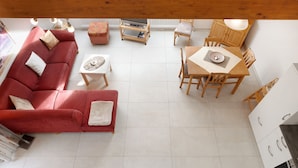 Ein Wohnzimmer mit rotem Sofa, einem Holzesstisch und einer Küchenzeile mit weißen Schränken.