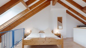 Ein Schlafzimmer mit schrägen Wänden, einem hölzernen Bett, Nachttischen und einem kleinen Spiegel.