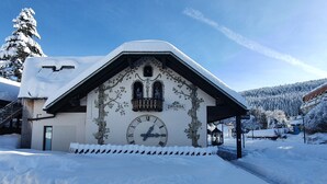 Ein Gebäude mit schneebedecktem Dach, einer großen Uhr und einem Schild mit der Aufschrift 'DRUBBA 1956'.