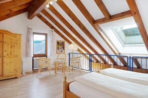 Une pièce avec un plafond en pente, des poutres en bois, un lit, des chaises en osier, une table, une armoire et une fenêtre donnant sur un paysage agréable.