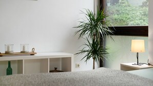 Een slaapkamer met een bed, een nachtkastje met een lamp, een potplant en een plank met kaarsen.