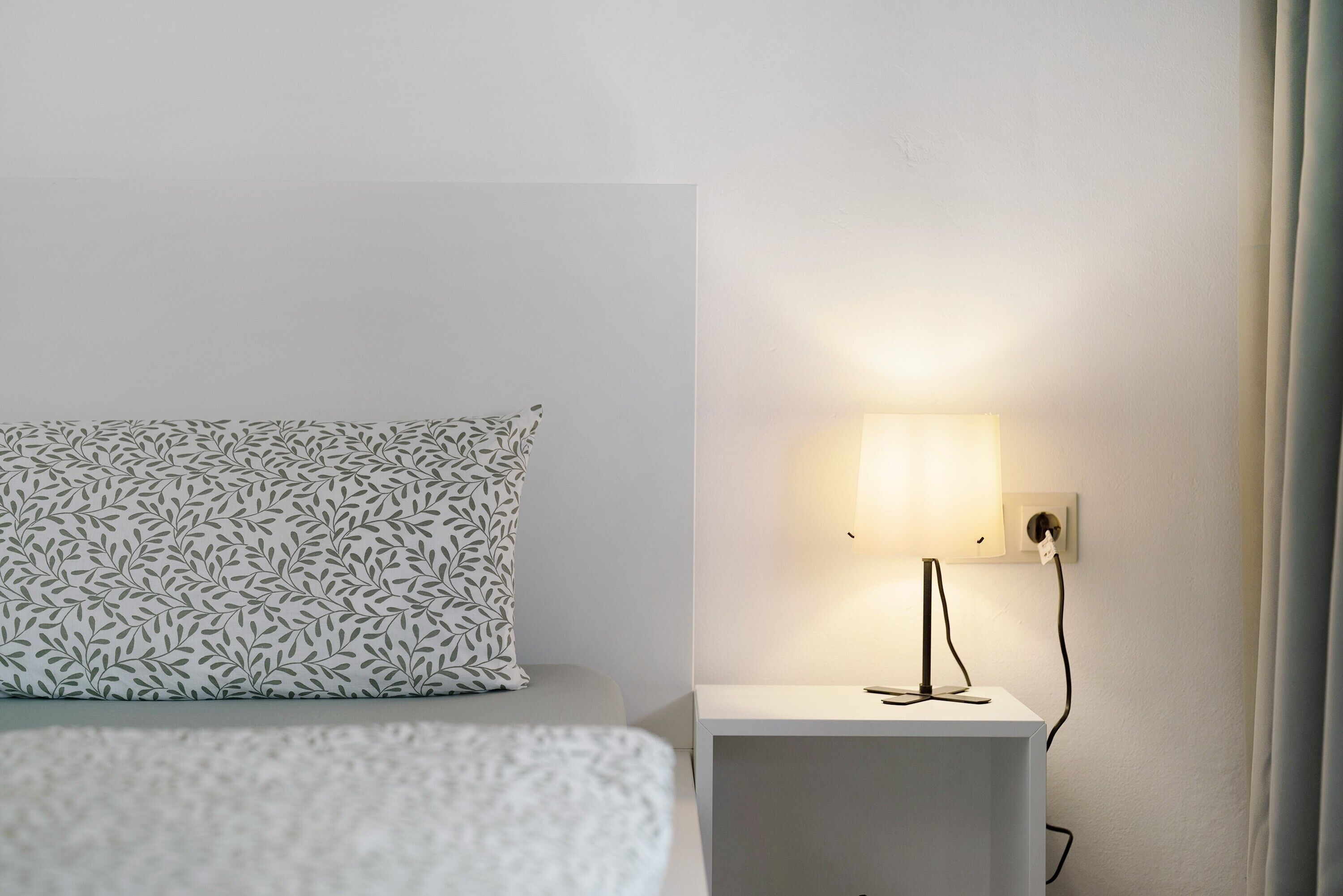Een bed met een gestreept kussen, een nachtkastje met een lamp en een stopcontact op de muur.