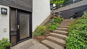 Een woongebouw met een zwarte deur, een klein buitenstuk met treden die naar een balkon leiden, en een potplant bij de ingang.