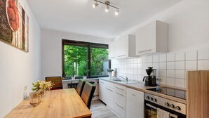 Een moderne keuken met witte kastjes, een houten eettafel en een groot raam.