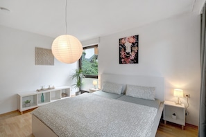 A bedroom with a bed, bedside tables, a hanging light, a window, and a wall with a geometric and floral artwork. - Apartment 'Am Lehen' with Mountain View, Private Terrace and Wi-Fi (Schiltach)