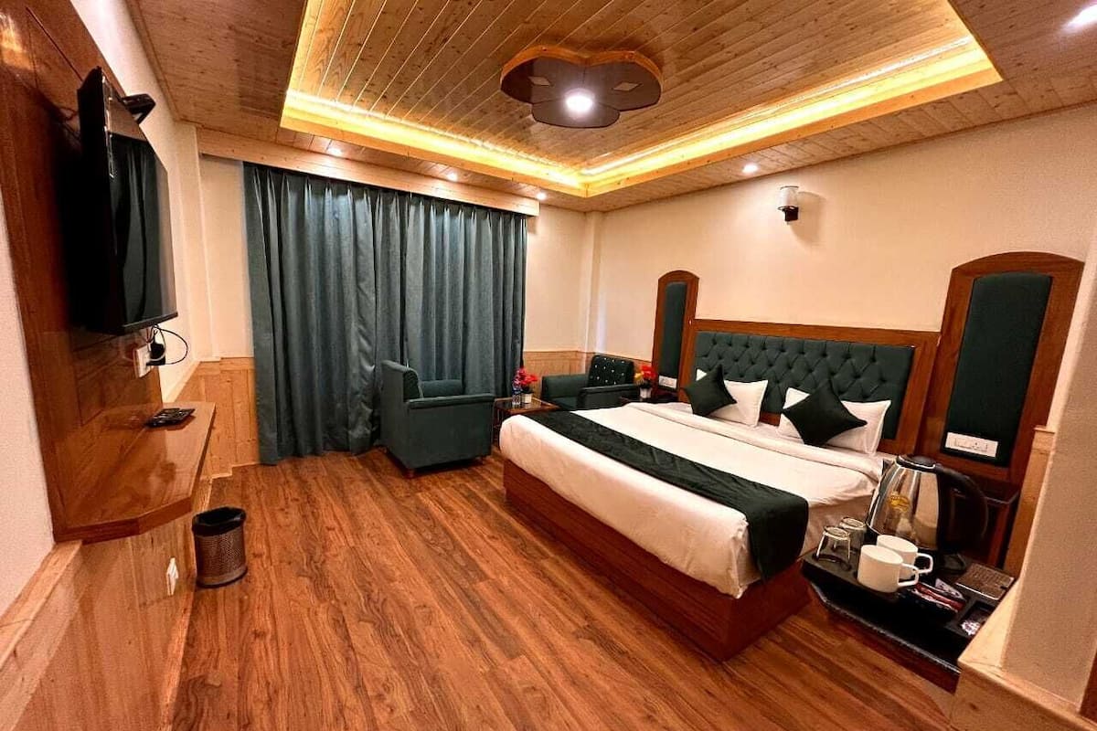 Una camera d'albergo con pavimento in legno, un letto grande con testiera imbottita, una TV a schermo piatto montata a parete e una scrivania con macchina del caffè e tazze.