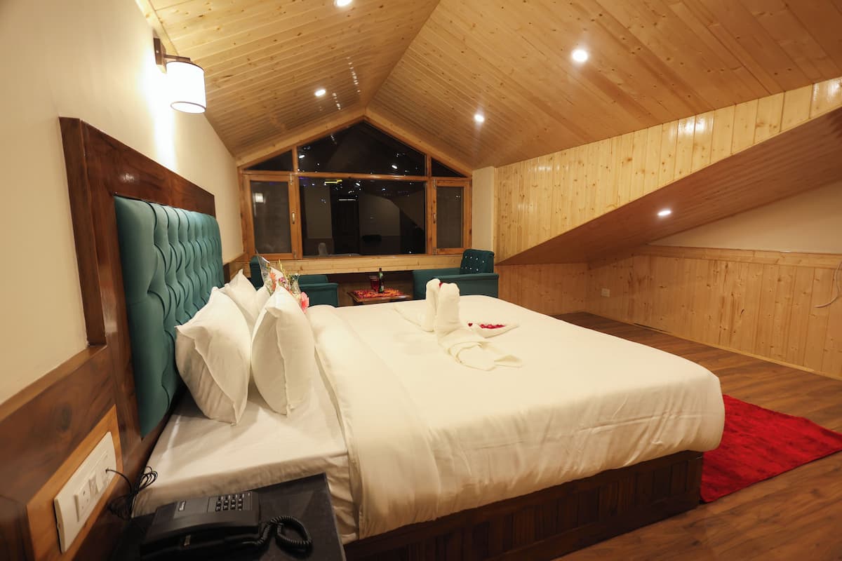 Camera d'albergo con soffitto in legno, un ampio letto con biancheria bianca, un tappeto rosso e una testiera in legno.