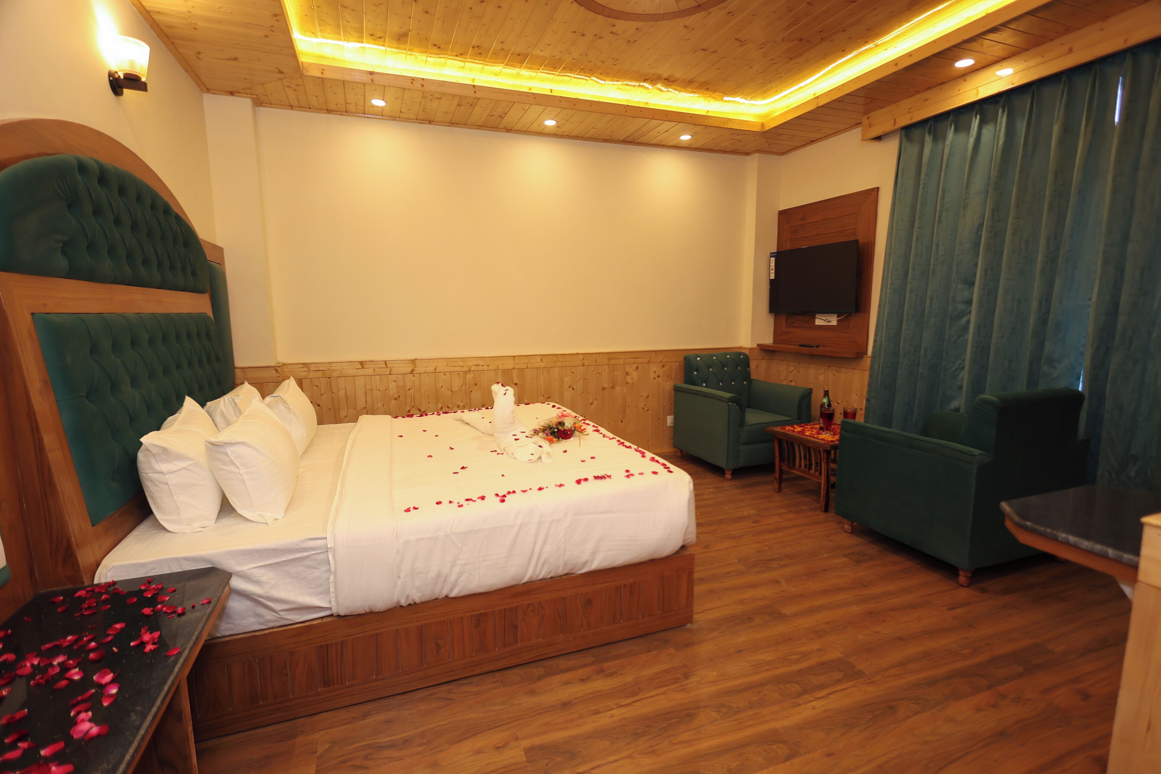 A hotel room with a large bed, a television mounted on the wall, a seating area with a table, and a wooden ceiling.
