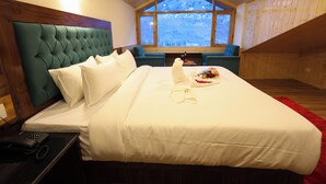 Un dormitorio con una cama grande, cabecera de madera, ventana con vistas a un paisaje nevado y una mesita con una botella y flores.