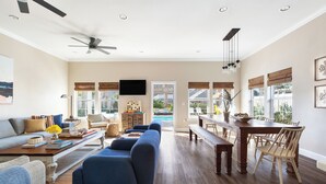 A spacious living room with a large sofa, a dining table with chairs, and a ceiling fan. - Sleeps 18! Private Pool, Hot Tub, Near Beach | Miramar Dream House by AvantStay (Miramar Beach)