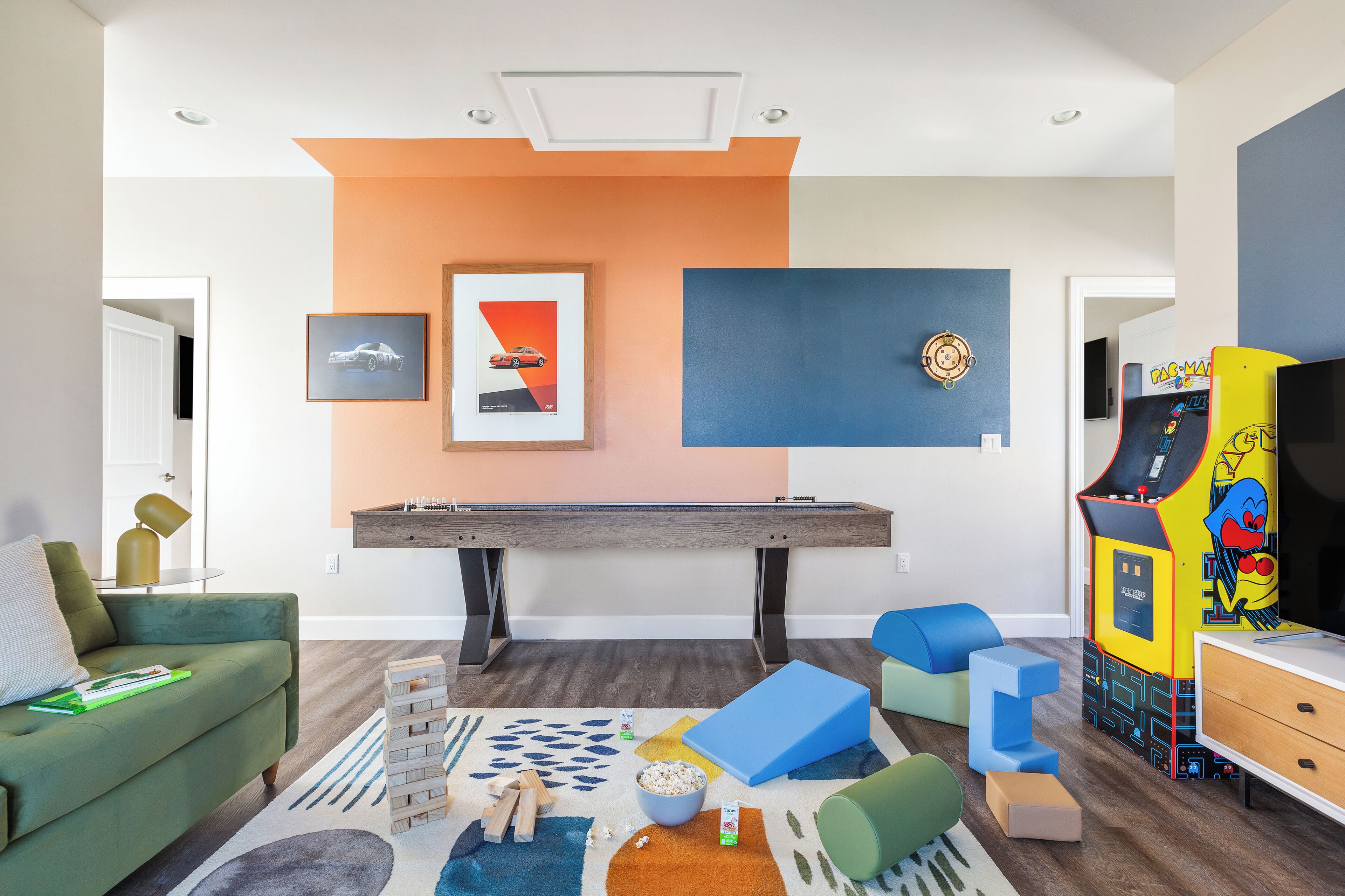 A modern living room with a pool table, green sofa, and colorful play area.