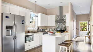 A modern kitchen with white cabinetry, stainless steel appliances, and a central island with stools. - Sleeps 18! Private Pool, Hot Tub, Near Beach | Miramar Dream House by AvantStay (Miramar Beach)