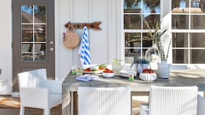 A dining area with a table set for four, surrounded by white wicker chairs, a wooden bench, and a small side table. - Sleeps 18! Private Pool, Hot Tub, Near Beach | Miramar Dream House by AvantStay (Miramar Beach)