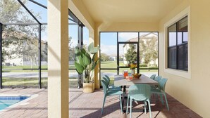 A covered patio with a table and chairs, a potted plant, and a view of a swimming pool and greenery.
