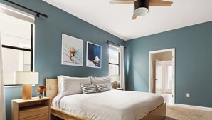 A bedroom with a bed, bedside tables, a ceiling fan, and artwork on the wall.