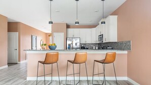 Una cocina moderna con una isla central, tres taburetes de bar e iluminación colgante.