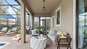 Un patio techado con piscina, sillas de descanso, una mesa y una parrilla.