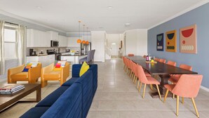 Une cuisine moderne avec des meubles blancs, un four à micro-ondes et un coin repas comprenant une longue table et des chaises orange.