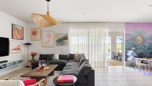 Una sala moderna con un sofá seccional gris grande, una mesa de centro de madera, un sillón de mimbre y un televisor de pantalla plana montado en la pared.