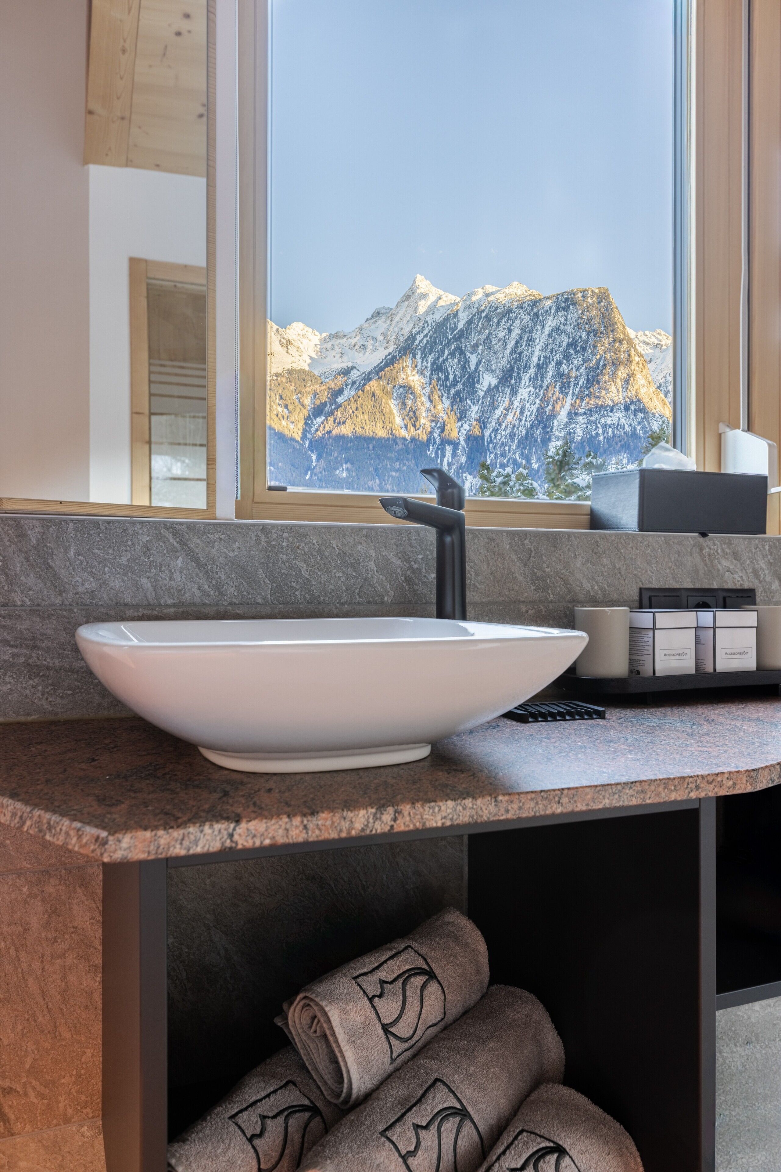 A modern bathroom with a large window, a white vessel sink, and neatly rolled towels.