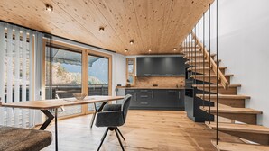 A modern kitchen with wooden flooring, a dining area with a table and chairs, and a staircase with glass railings. - See the Holiday Home with Lake View, Private Terrace and Wi-Fi (Oetz)