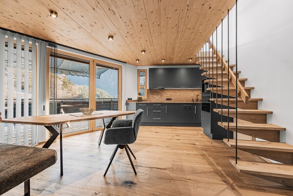 A modern kitchen with wooden flooring, a dining area with a table and chairs, and a staircase with glass railings. - See the Holiday Home with Lake View, Private Terrace and Wi-Fi (Oetz)