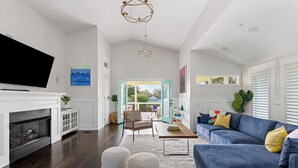 A modern living room with a fireplace, a blue sofa, and a large TV. - Luxe Villa near Beach, Pool + HotTub, Chef's Kitchen | Woodward Way by AvantStay (Destin)