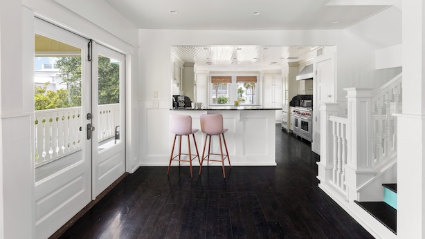 A modern kitchen with white cabinetry, a dark wood floor, and two pink bar stools. - Luxe Villa near Beach, Pool + HotTub, Chef's Kitchen | Woodward Way by AvantStay (Destin)