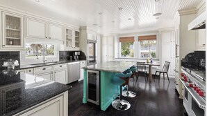 A kitchen with white cabinets, a teal island, and a dining area with chairs. - Luxe Villa near Beach, Pool + HotTub, Chef's Kitchen | Woodward Way by AvantStay (Destin)