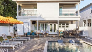 Una casa de dos pisos con piscina, mobiliario exterior y un patio.