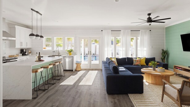 Una cocina moderna con armarios blancos, una isla central con taburetes de bar y una zona de comedor con un sofá azul oscuro y una mesa de centro redonda de madera.