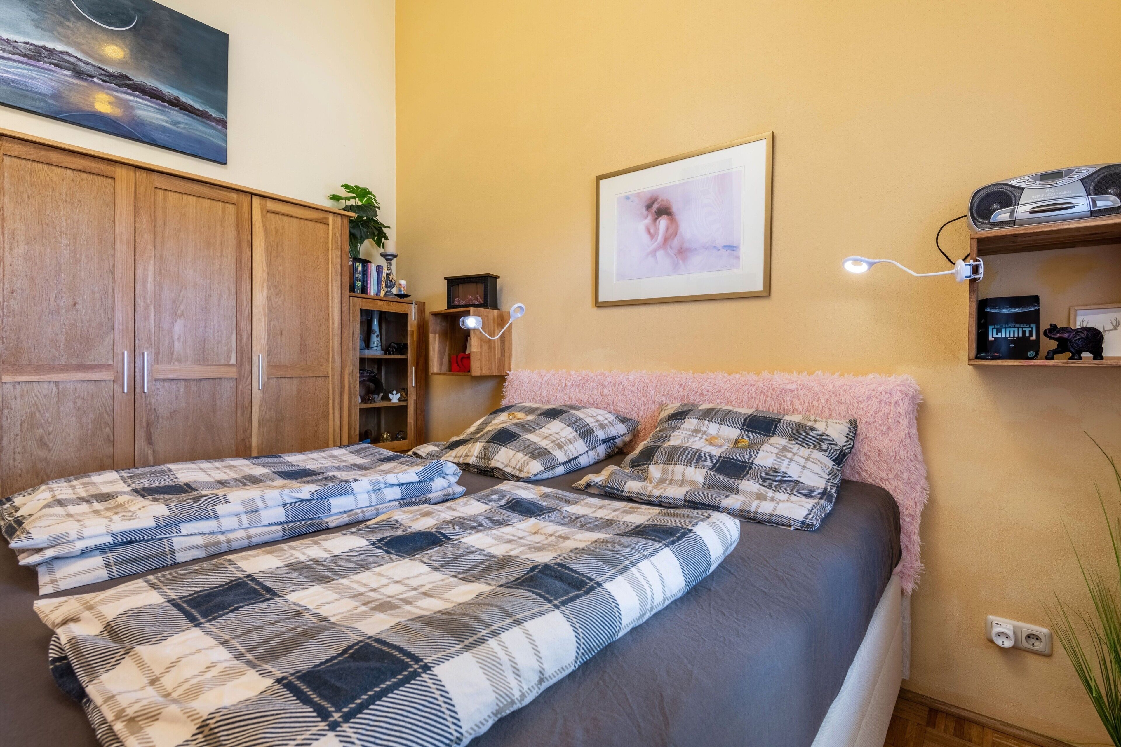 Un dormitorio con cama, armario, estante con objetos y un cuadro en la pared.