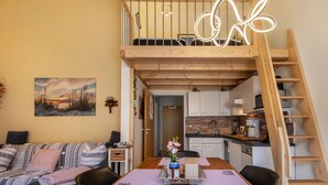 A loft-style apartment with a dining area, kitchen, and a wooden staircase.