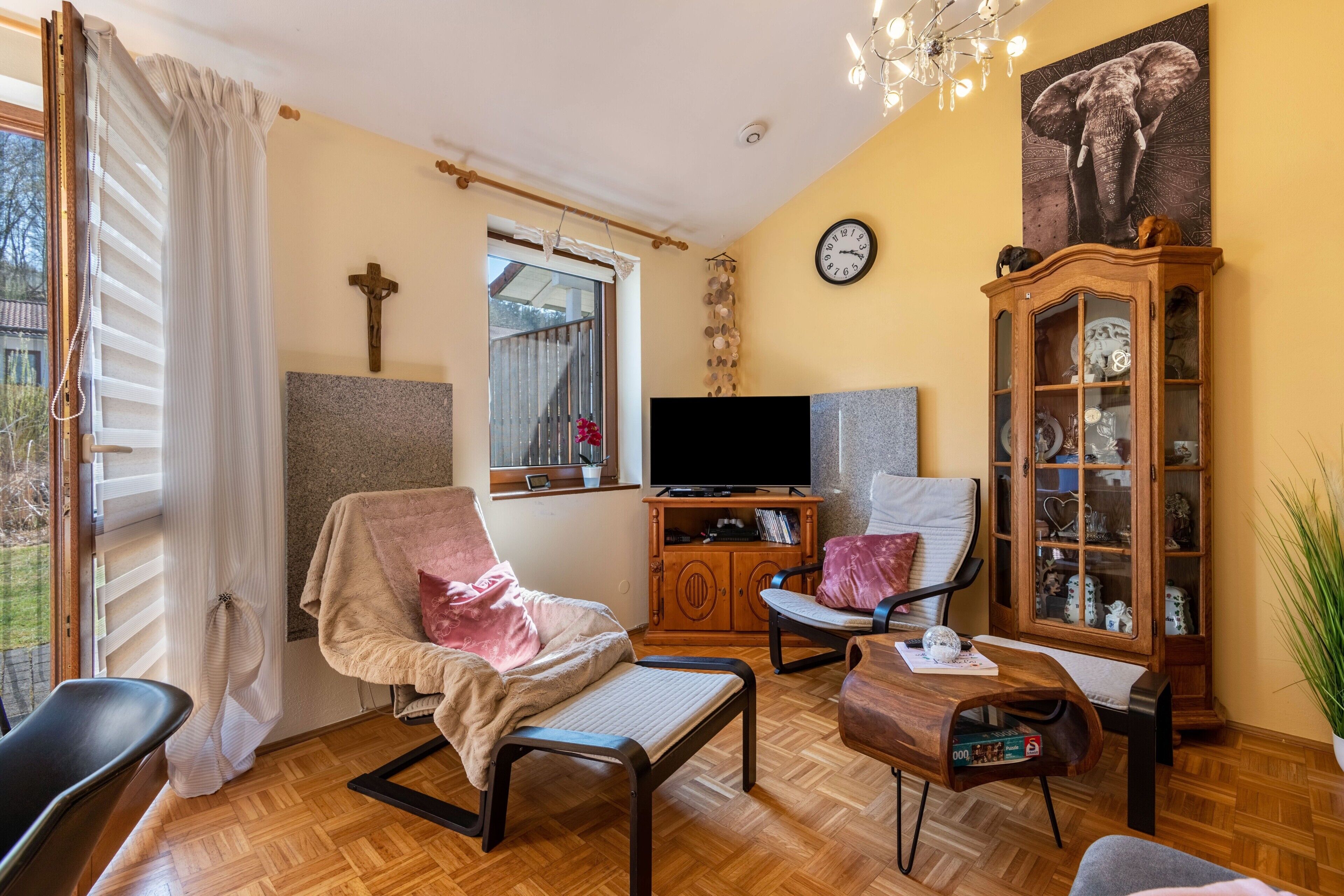 A living room with a TV, wooden cabinet, and a large elephant painting.