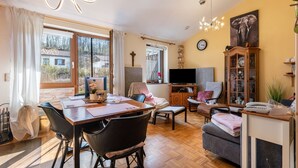 A living room with a dining area, a television, a cabinet with decorative items, and a large window with curtains.