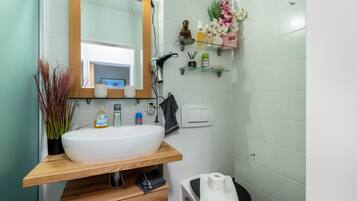 Une salle de bain avec un lavabo blanc, un meuble-lavabo en bois, un miroir et une petite étagère contenant des articles de toilette.