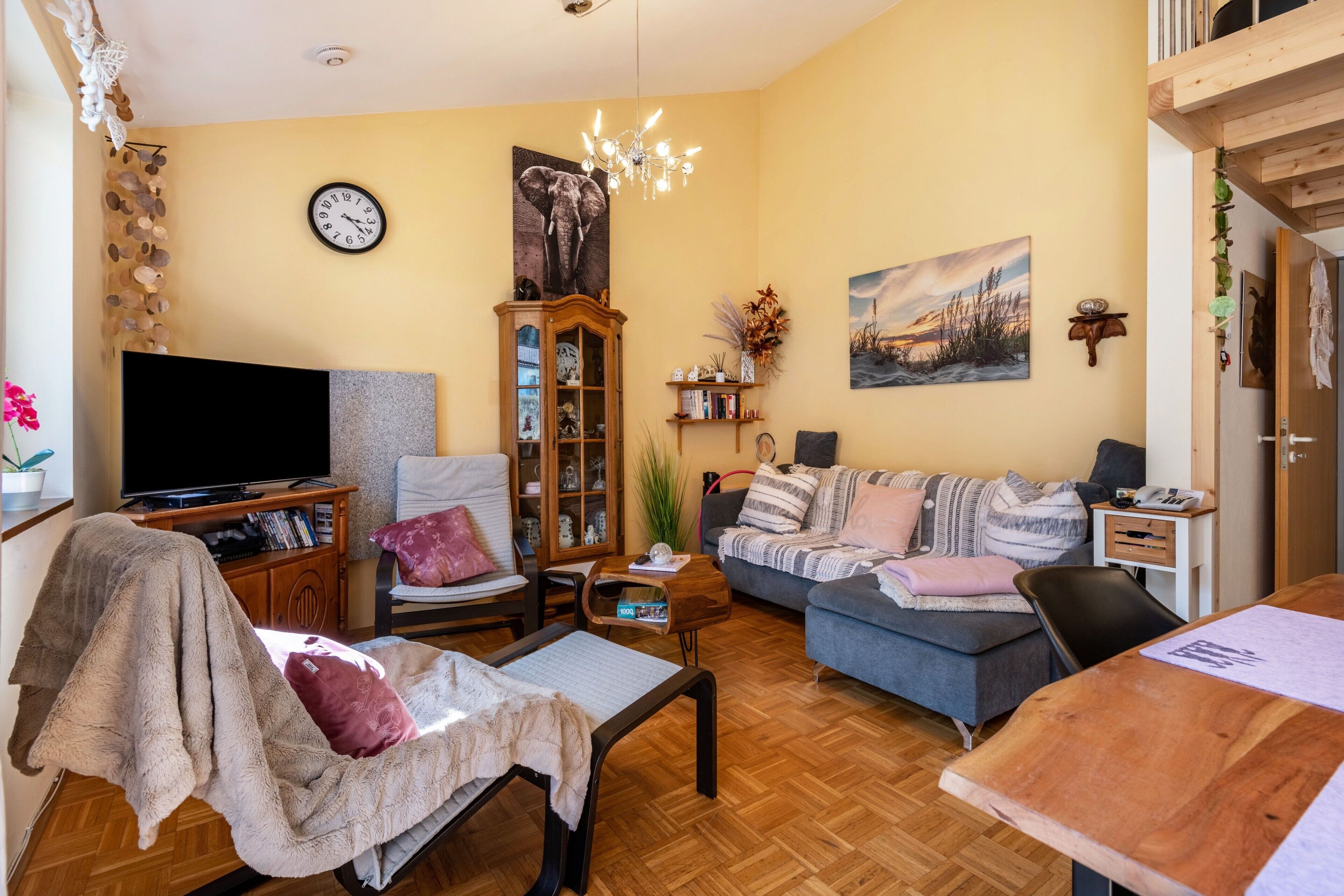 Ein Wohnzimmer mit Fernseher, Sofa, Sessel, Couchtisch aus Holz und Bücherregal.