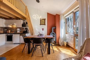 Una cocina moderna con vigas de madera, un comedor con mesa y sillas, y un amplio ventanal con cortinas.