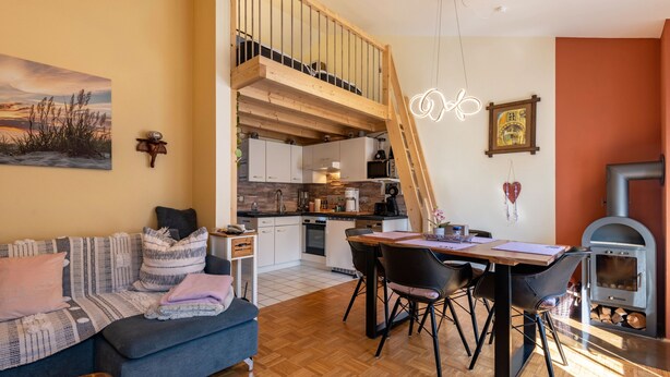 A cozy living room with a sofa, a dining table with chairs, a kitchen area, a loft bedroom, and a fireplace.